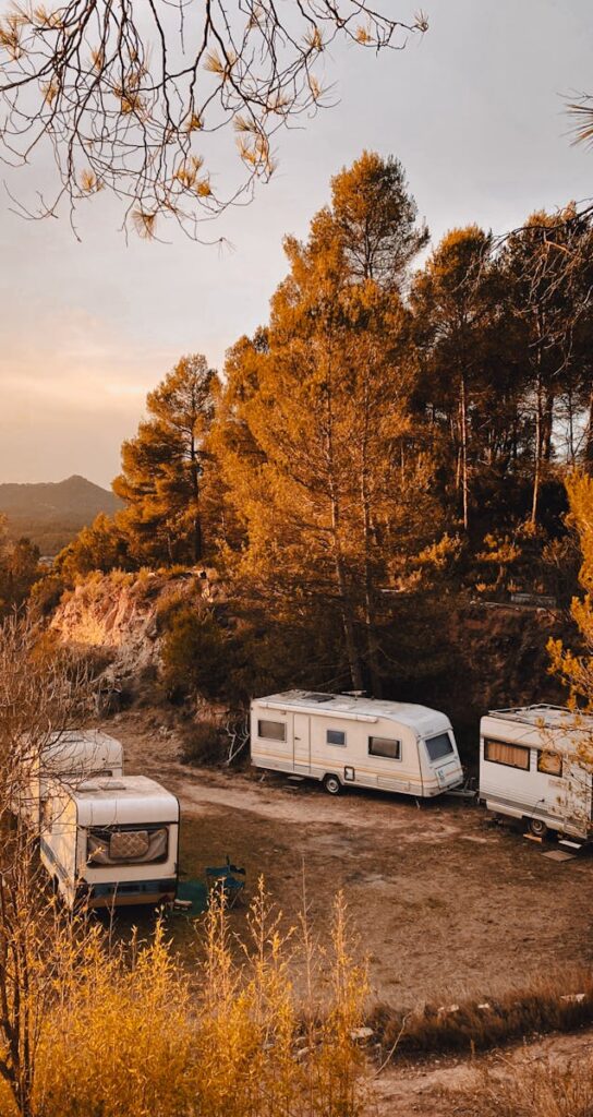 Caravans parked amidst trees in Sant Salvador de Guardiola, Spain during a serene sunset.