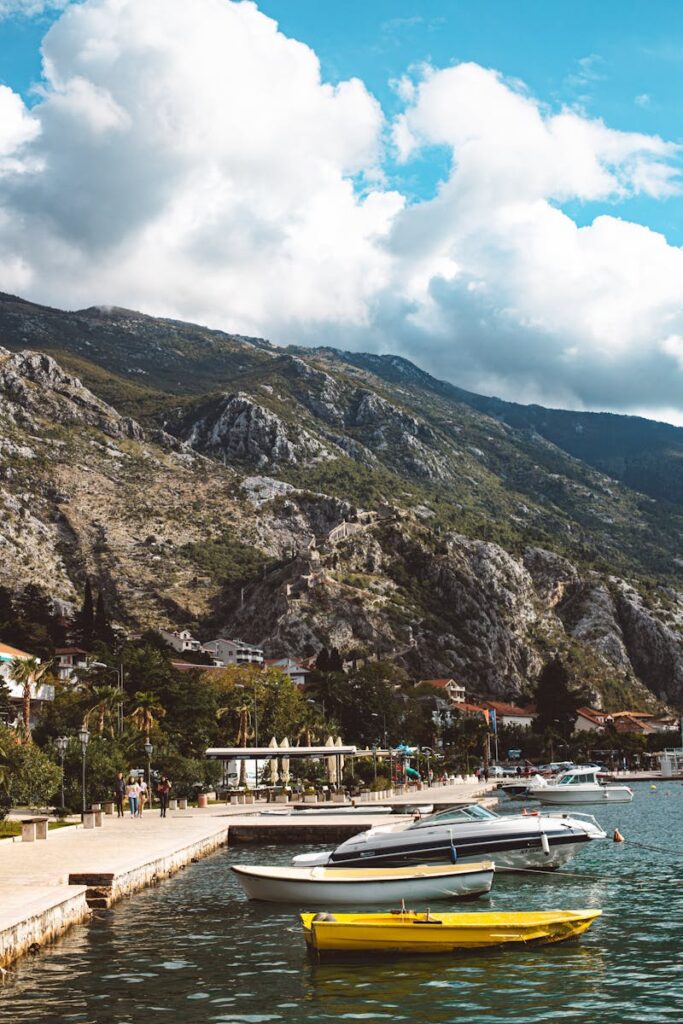 Peaceful mountain lake with docked boats, rocky backdrop, and blue sky.