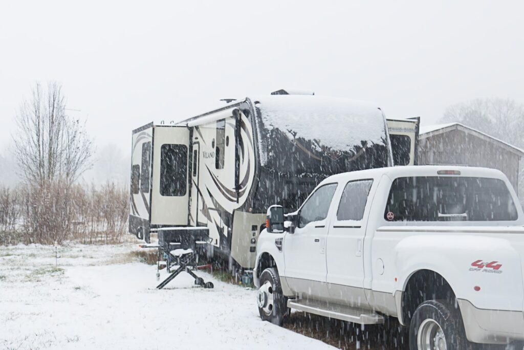 A white truck parked next to a trailer in the snow