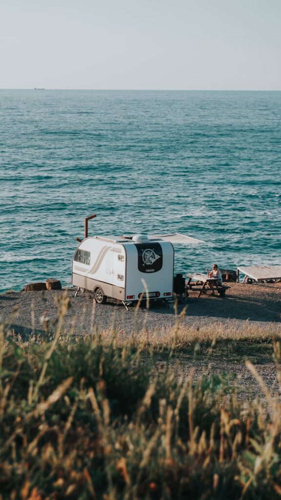 Enjoy a peaceful camping experience by the sea with a parked camper and picnic setup.