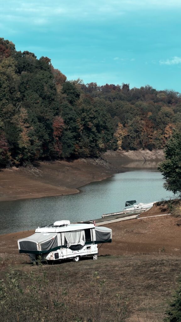 Pop-up camper parked by a calm lake with wooded hills.