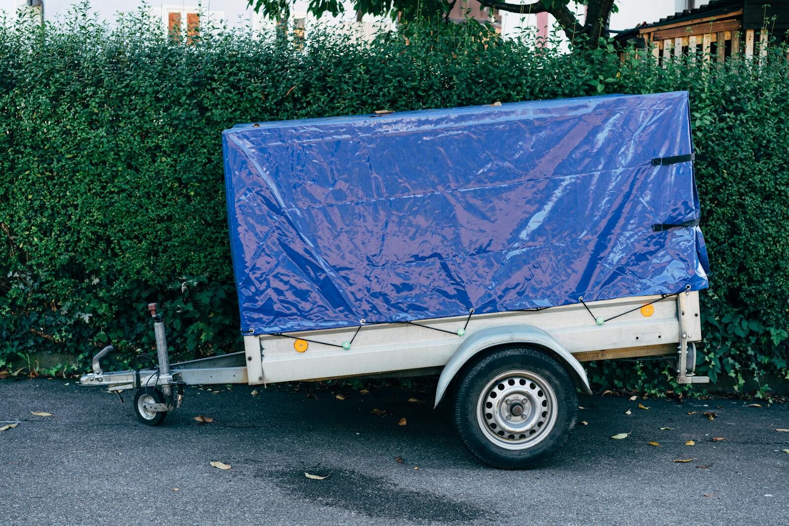 Photo by Markus Winkler A blue tarpaulin-covered trailer parked on a roadside against a hedge, ideal for transport themes.
