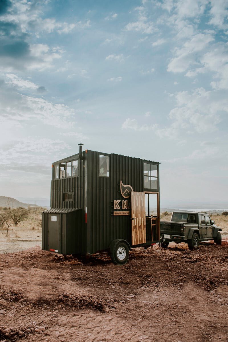 Photo by Amar Preciado An off-road vehicle towing a mobile trailer in a vast desert landscape under a cloudy sky.