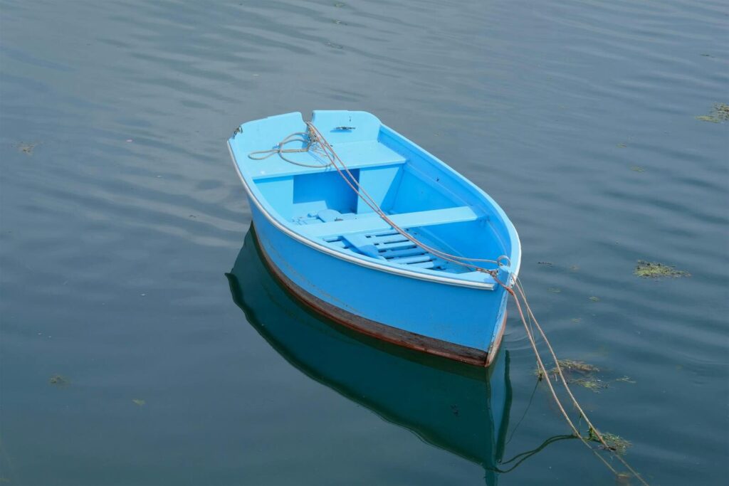 A tranquil scene of a vibrant blue wooden boat gently floating on serene lake waters.