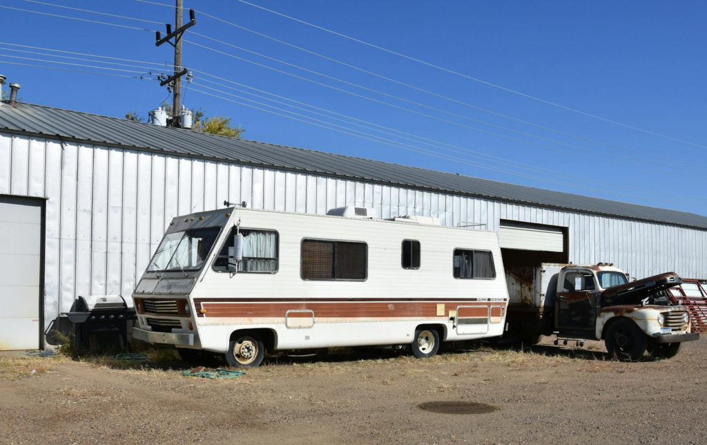 Classic RV parked beside a metal warehouse under a clear blue sky in Glasgow, Montana. Perfect for travel and lifestyle themes.