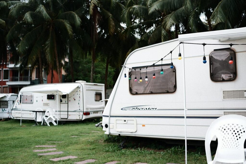 Relaxing caravan camping site under palm trees with outdoor seating and festive lights.