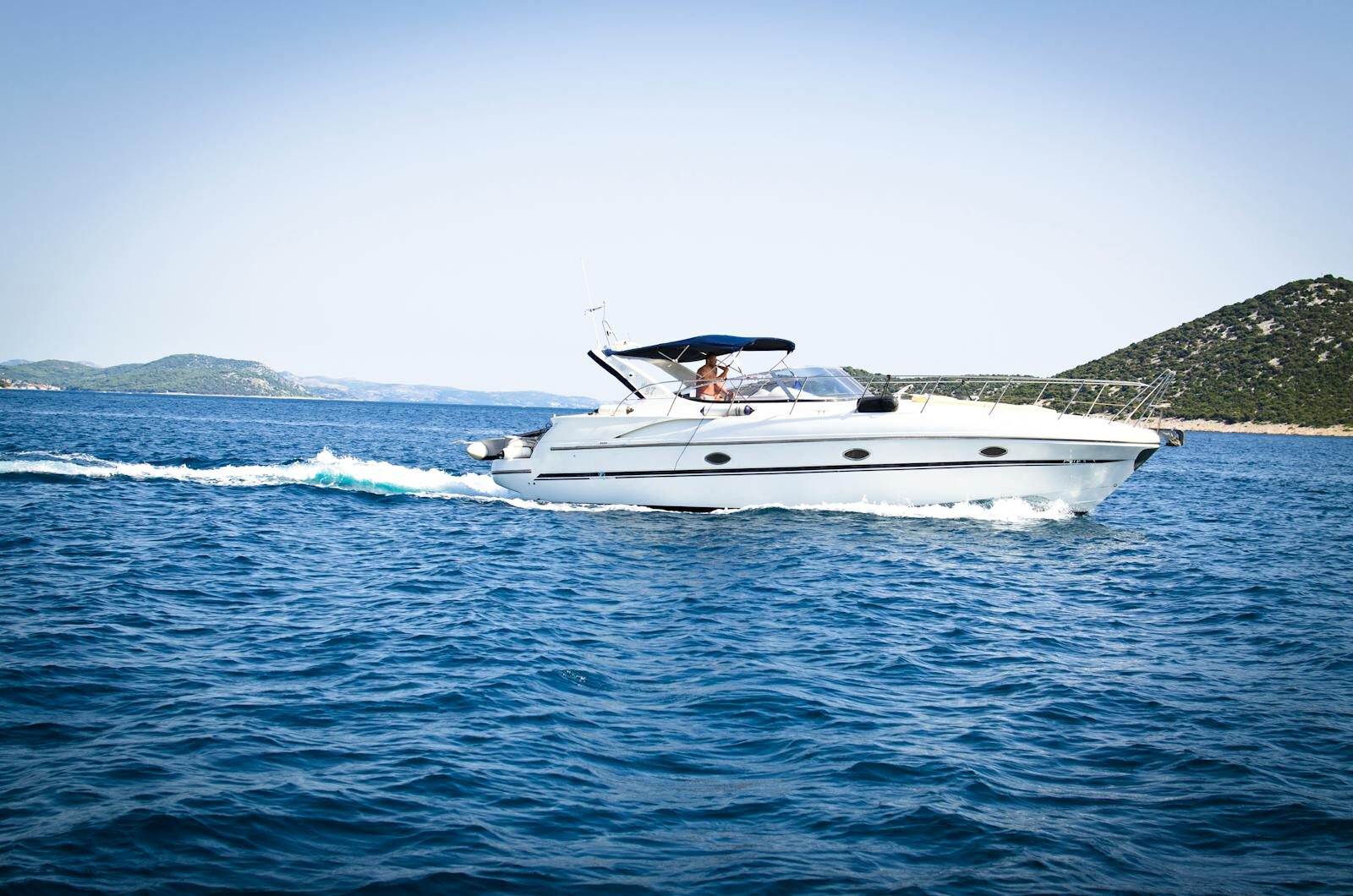 Photo by Lukas Blazek A sleek white yacht cuts through the open sea under a clear blue sky, capturing relaxation and travel.
