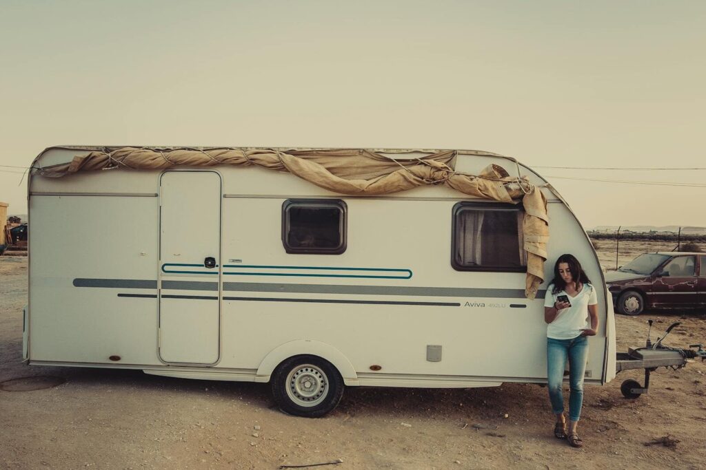 A woman stands by a camper van in a serene outdoor setting during sunset.