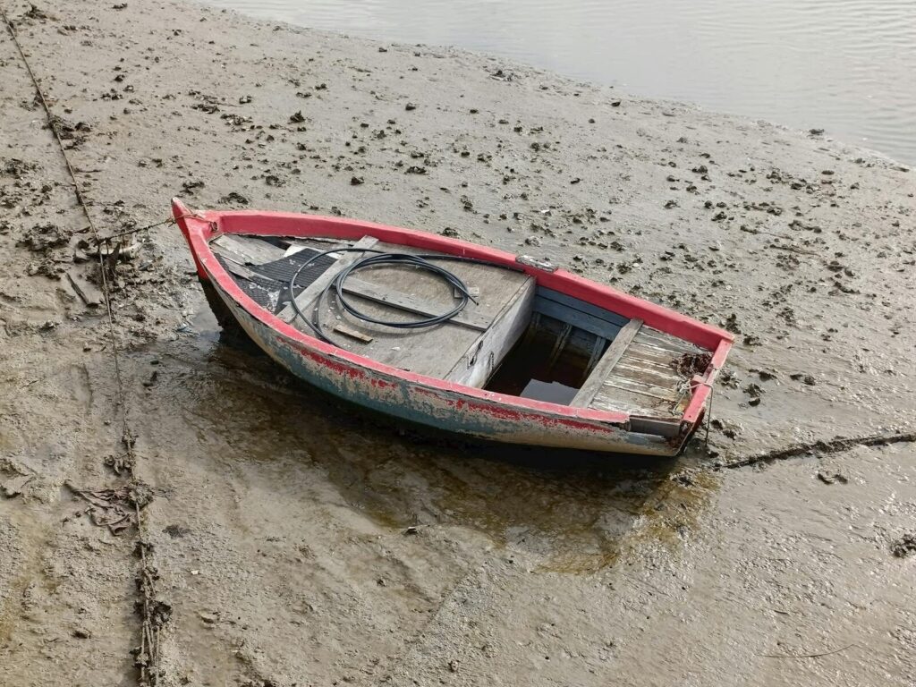 A small wooden boat rests on a muddy riverbank in El Puerto de Santa María, Spain.
