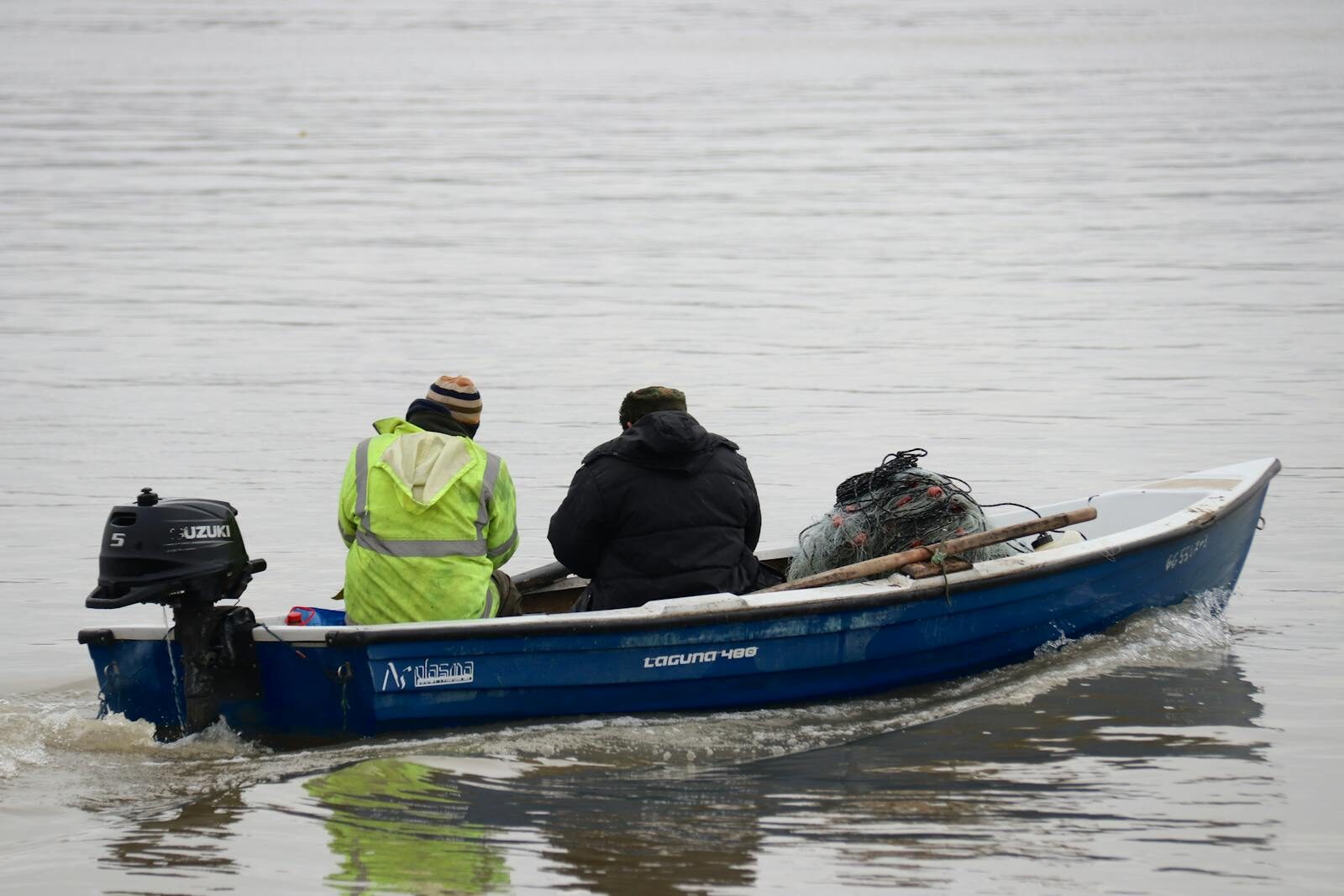 Two men fishing on a small blue boat with nets in calm water, captured from behind.