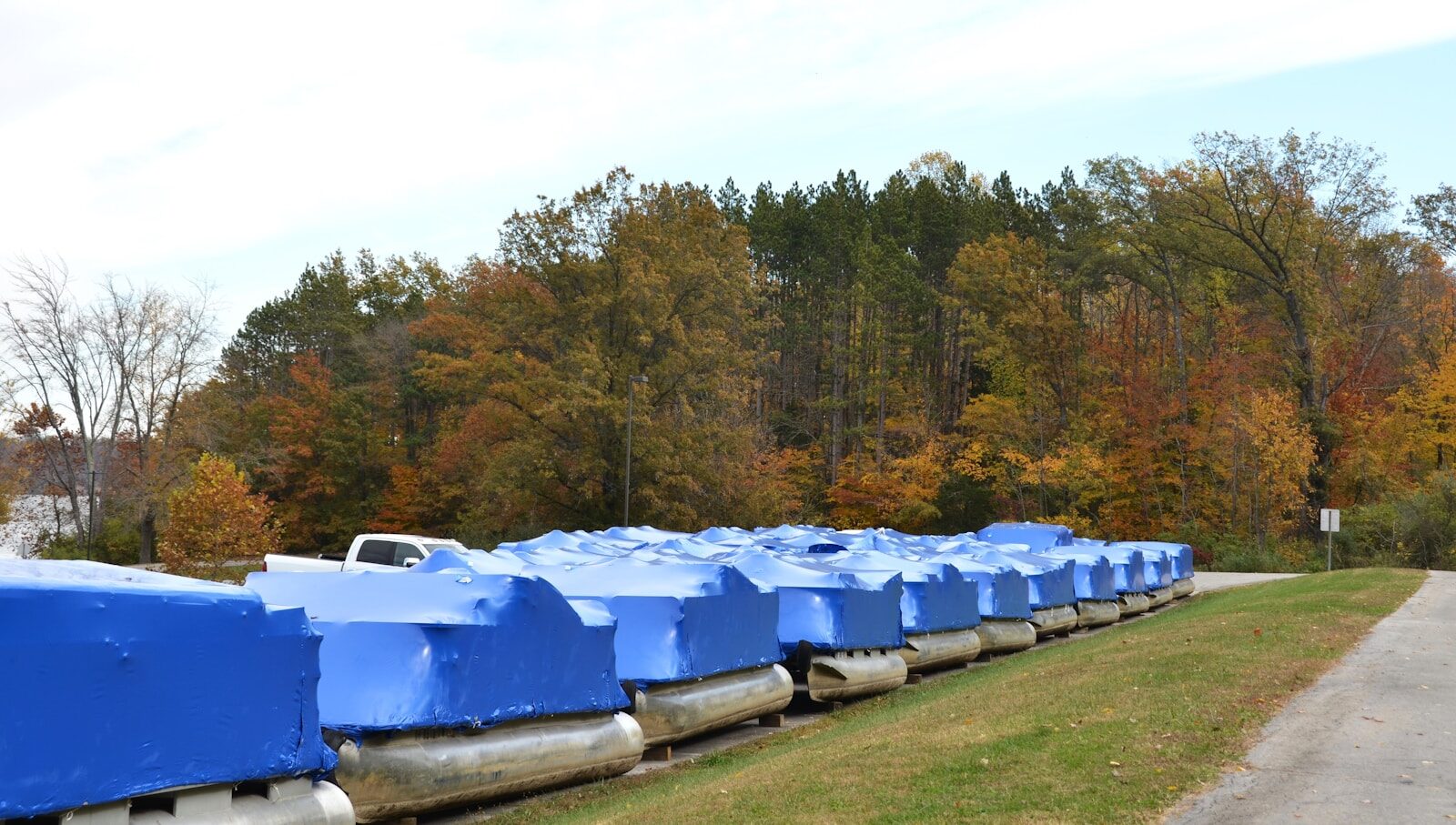 Boats covered in blue tarps with autumn trees behind.