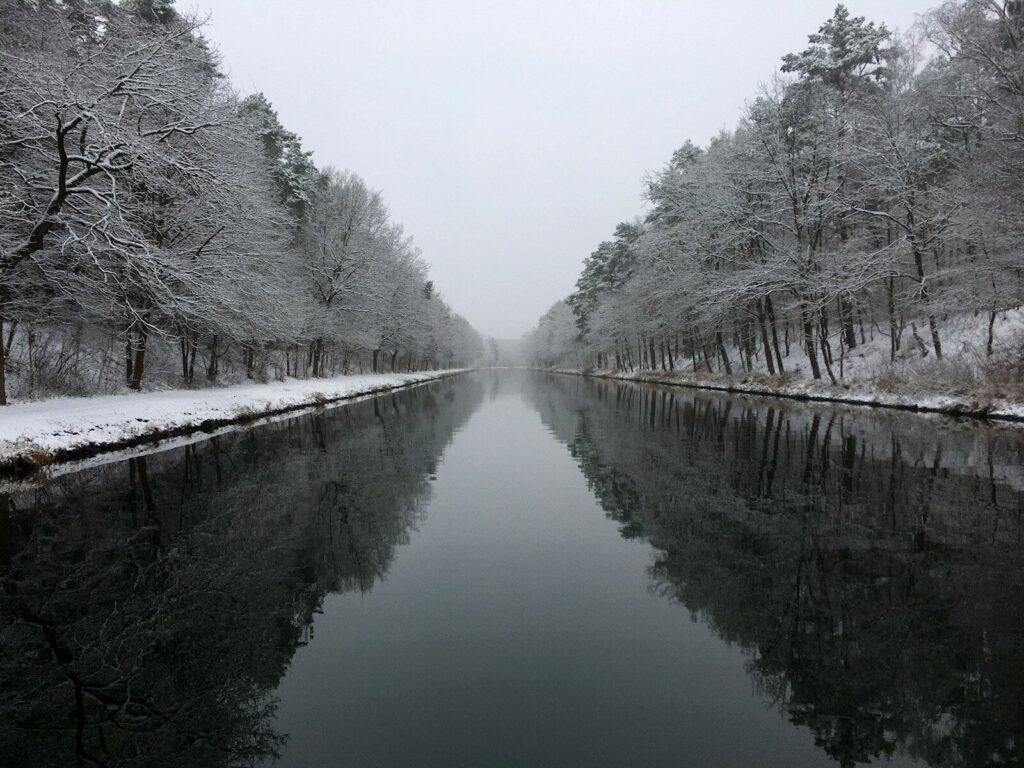 a body of water with snow on the side and trees around it
