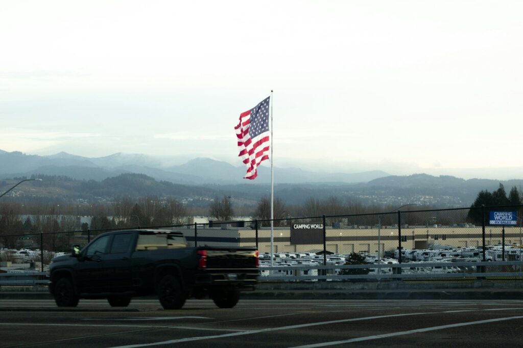 American flag waves near a dark truck and mountains.