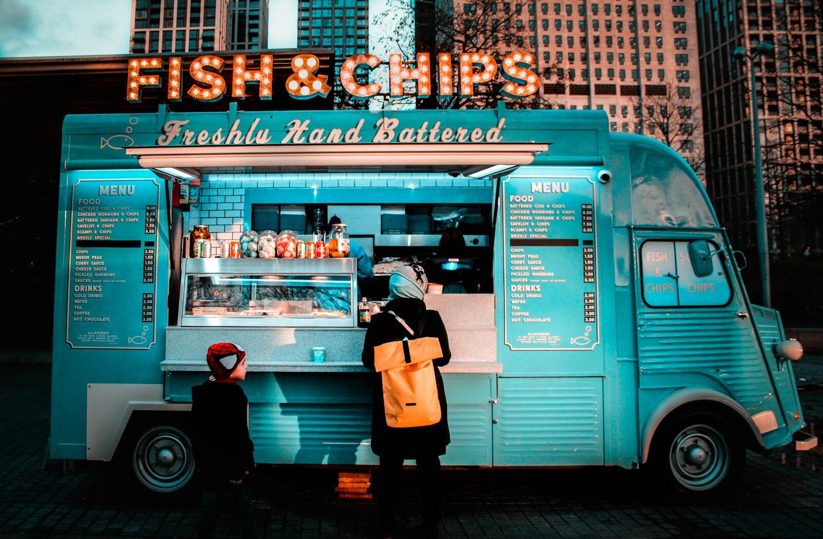 Photo by Joana Godinho woman in brown coat standing in front of food stall