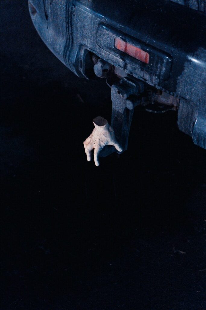 A small hand hangs from a car's trailer hitch.