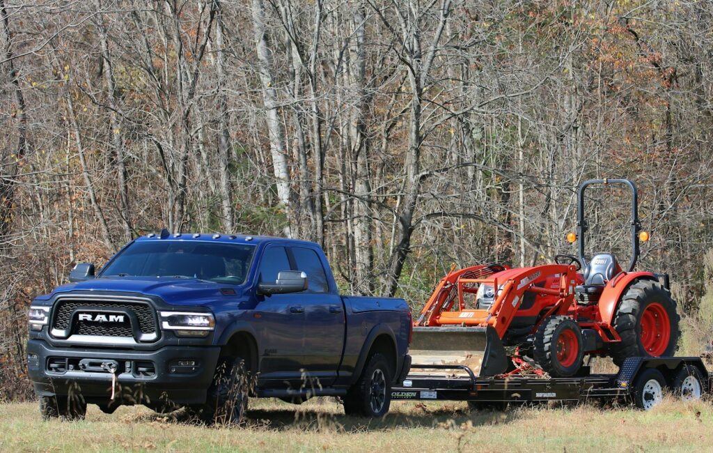 a blue pickup truck towing a red tractor