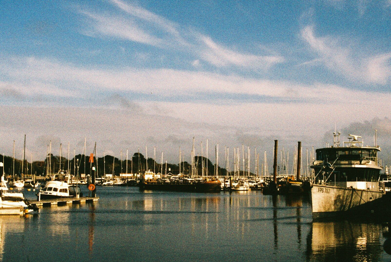 Boats docked in a sunny harbor with cloudy sky.