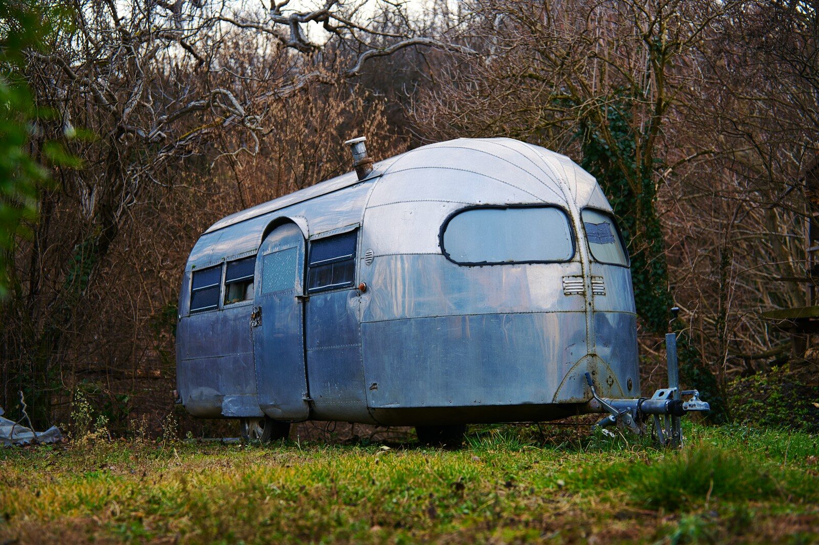 Vintage silver travel trailer parked in grassy field.