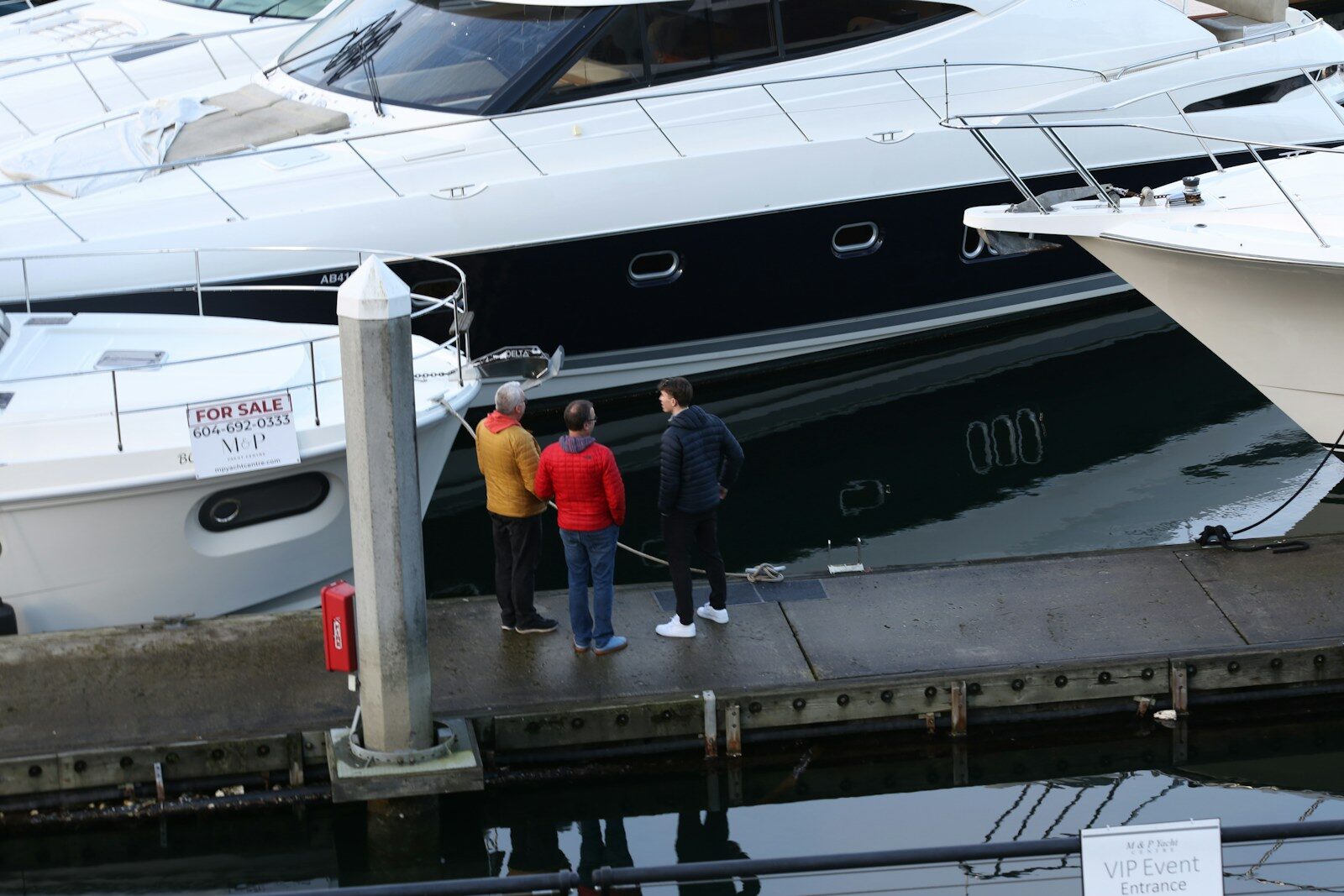 Photo by Veronica Dudarev Three people stand on a dock next to yachts.