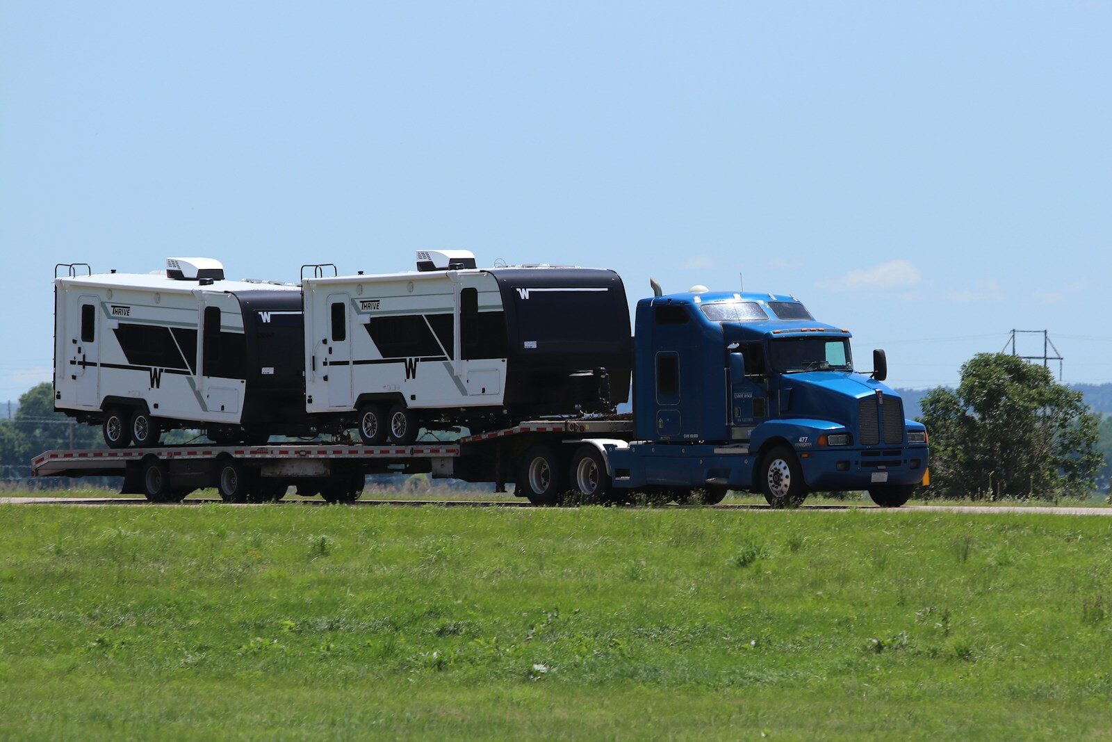 Photo by Preston A Larimer Blue semi-truck hauling two campers on a flatbed trailer.