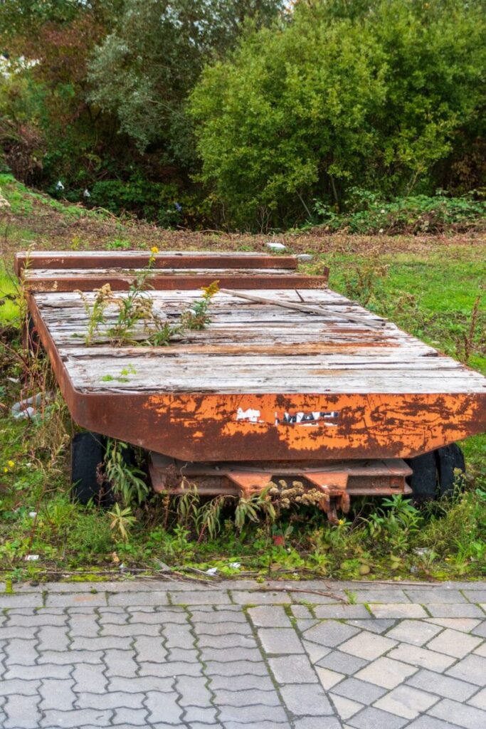 Old rusty flatbed trailer overgrown with weeds