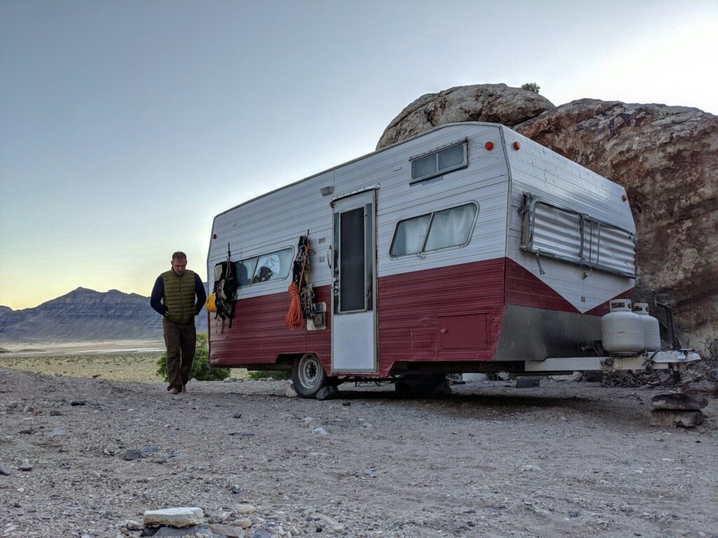 man in black jacket standing beside white and brown rv trailer during daytime