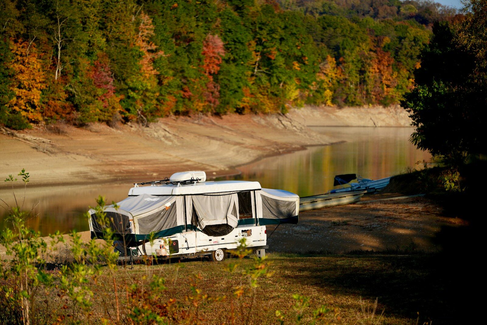 Pop-up camper parked by a calm lake in autumn.