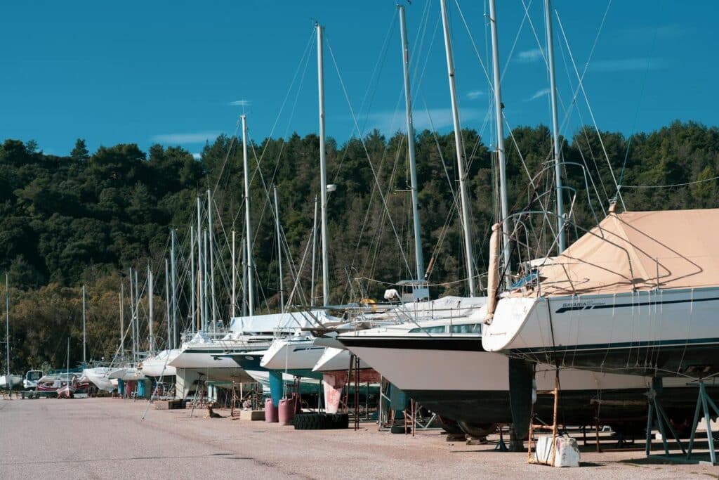 A row of sailboats in dry dock surrounded by lush green forest under a clear blue sky.