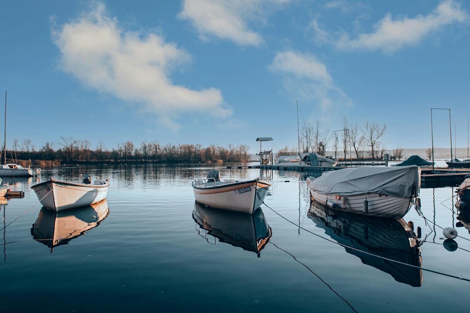 Peaceful lakeside scene with boats in a calm harbor at sunrise. Different Types of Boats and Why You Should Know Before You Buy
