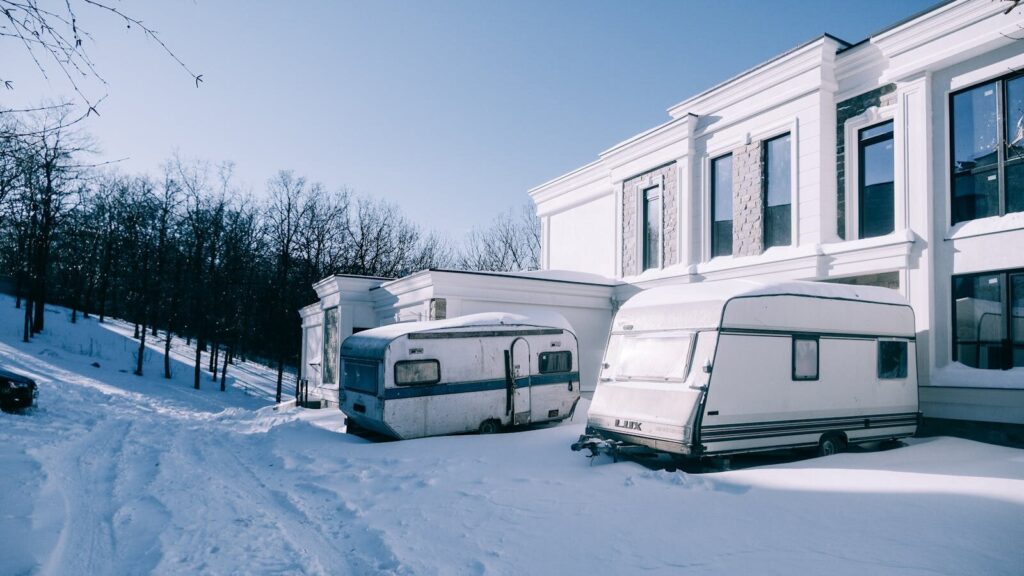 White trailers parked beside a snow-covered building under a clear blue sky, evoking winter tranquility.