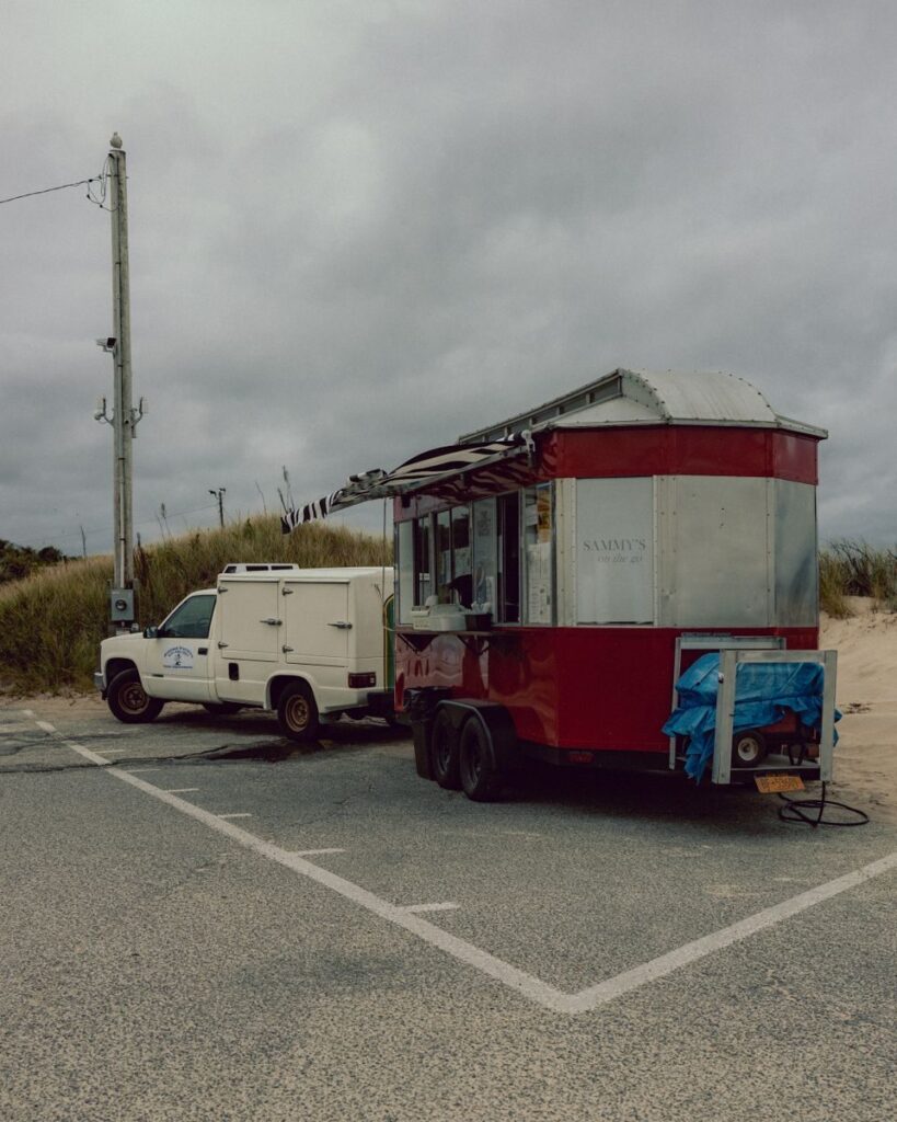 A red vintage food truck parked near the beach on a cloudy day.