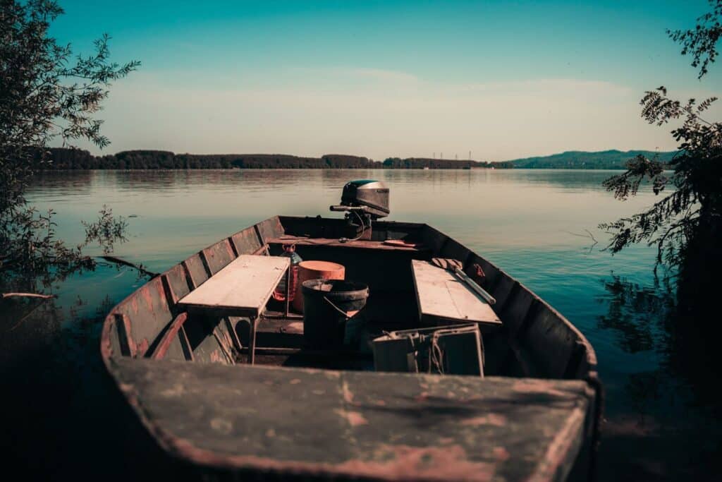 Discover serenity with this vintage motorboat docked at a calm lake, framed by lush greenery under a blue sky.