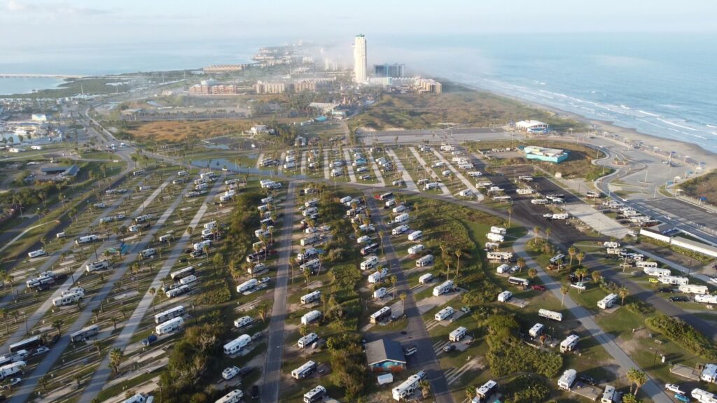 Aerial view of a coastal RV park near the ocean, showcasing numerous caravans and nearby resort buildings.