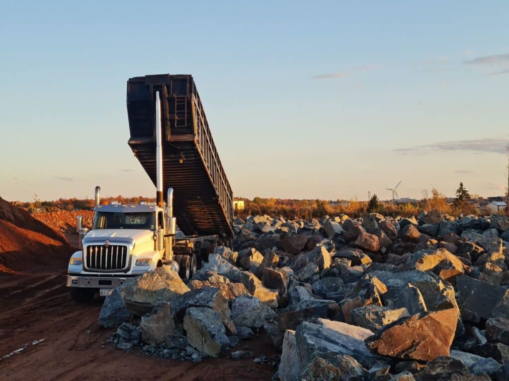 A dump truck unloading rocks at an outdoor quarry site during sunset.