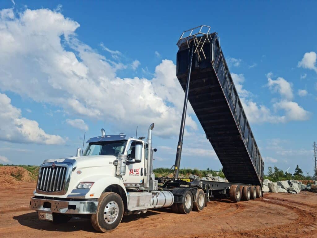 A large dump truck unloading at a construction site under a clear blue sky.