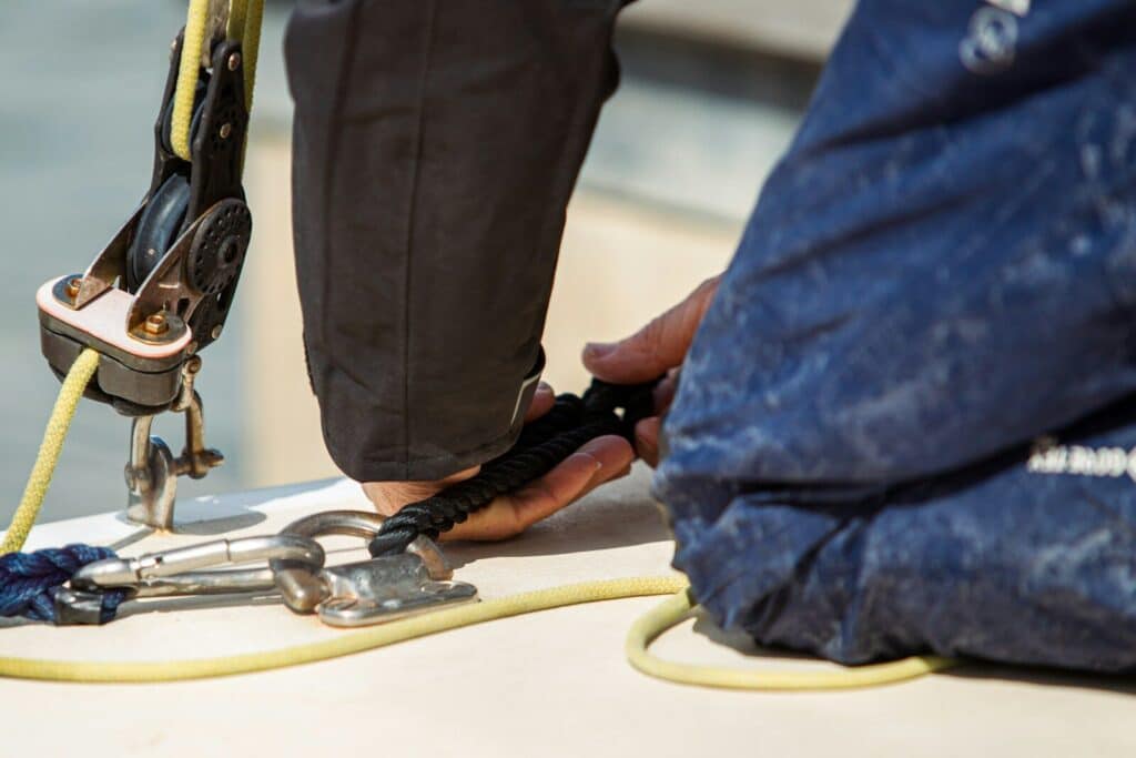 Hands adjusting sailing gear and ropes on a boat deck.