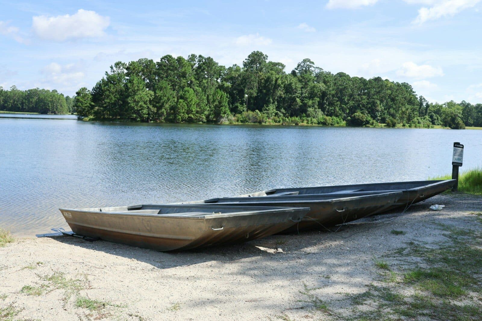 Photo by Synthia Hawkes Two boats on sandy shore by a calm lake. Your Ultimate Guide to Buying a Jon Boat This Summer with Interstate Haulers
