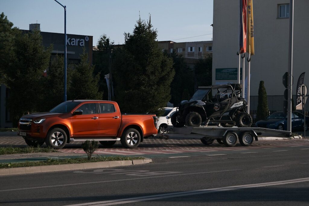 An orange pickup truck towing a black off-road vehicle on a trailer