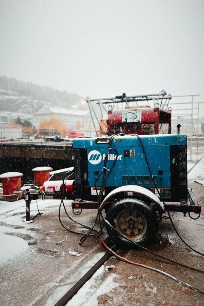 Industrial generator on wheels in a snowy outdoor environment with equipment backdrop.