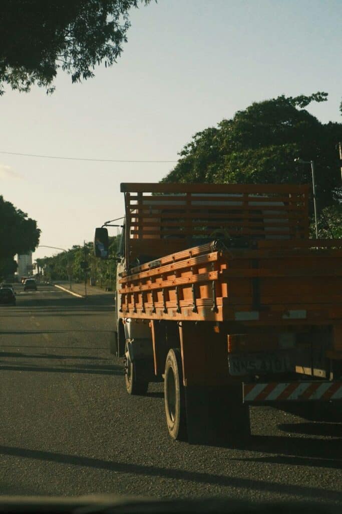 An orange flatbed truck driving on a road during the golden hour